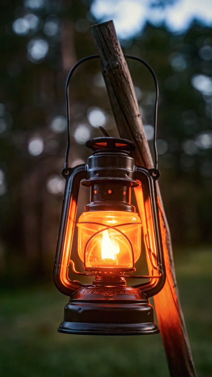 A glowing vintage lantern hanging on a wooden stick outdoors during twilight.